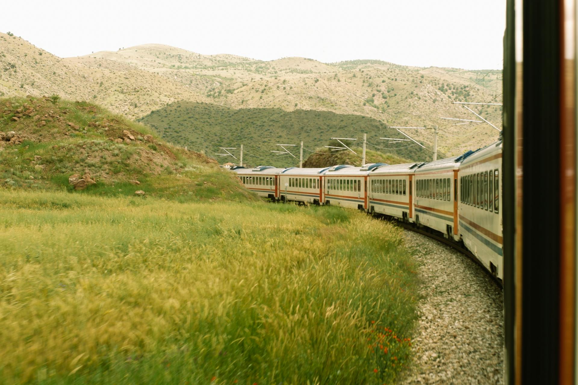 A train curving through lush green hills and meadows, offering a scenic travel experience.