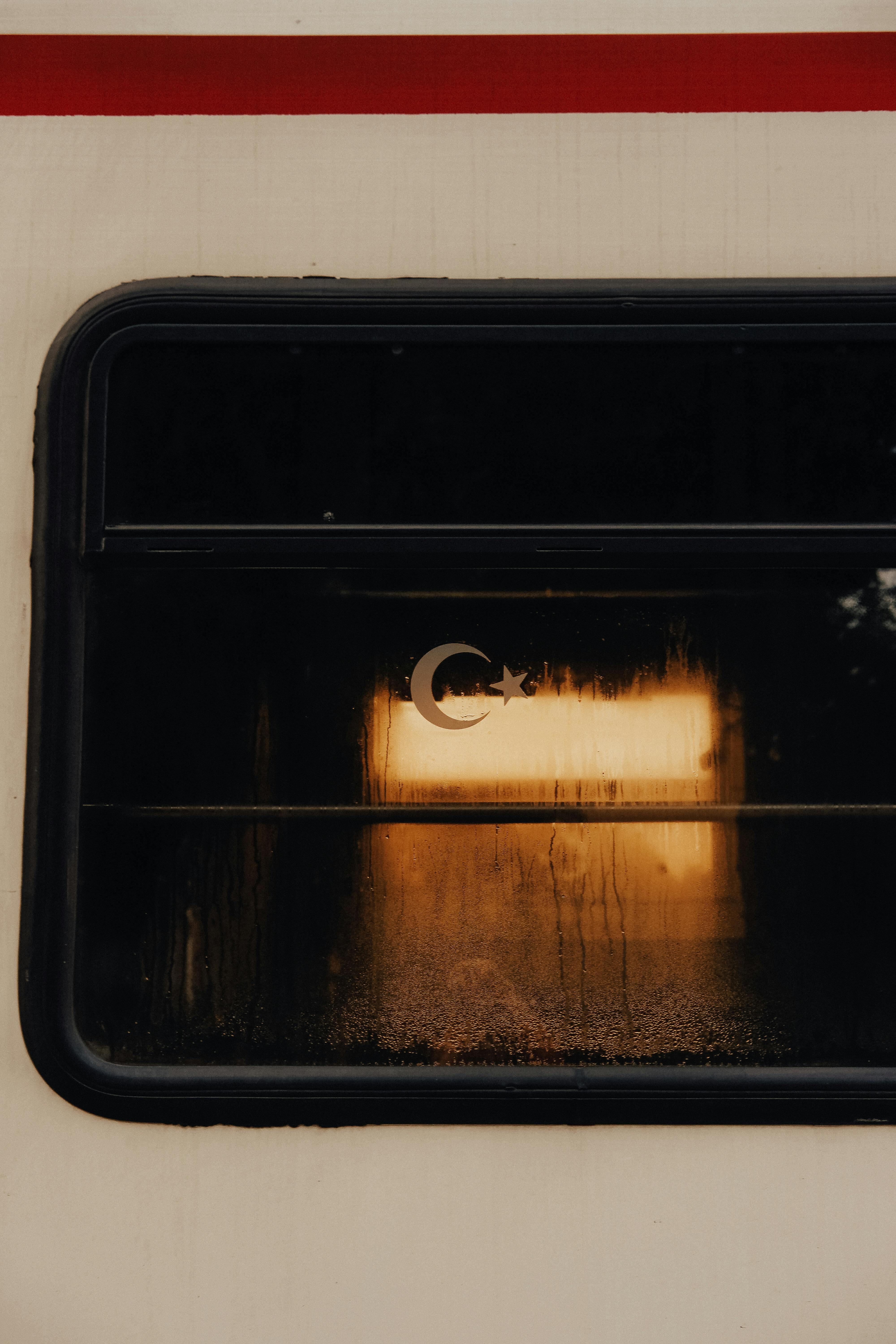 Moody train window with Turkish crescent reflecting warm sunset light.