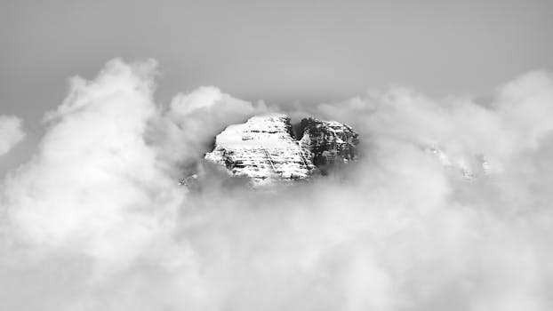 A striking view of a snow-covered mountain peak surrounded by dense clouds, showcasing nature's beauty.