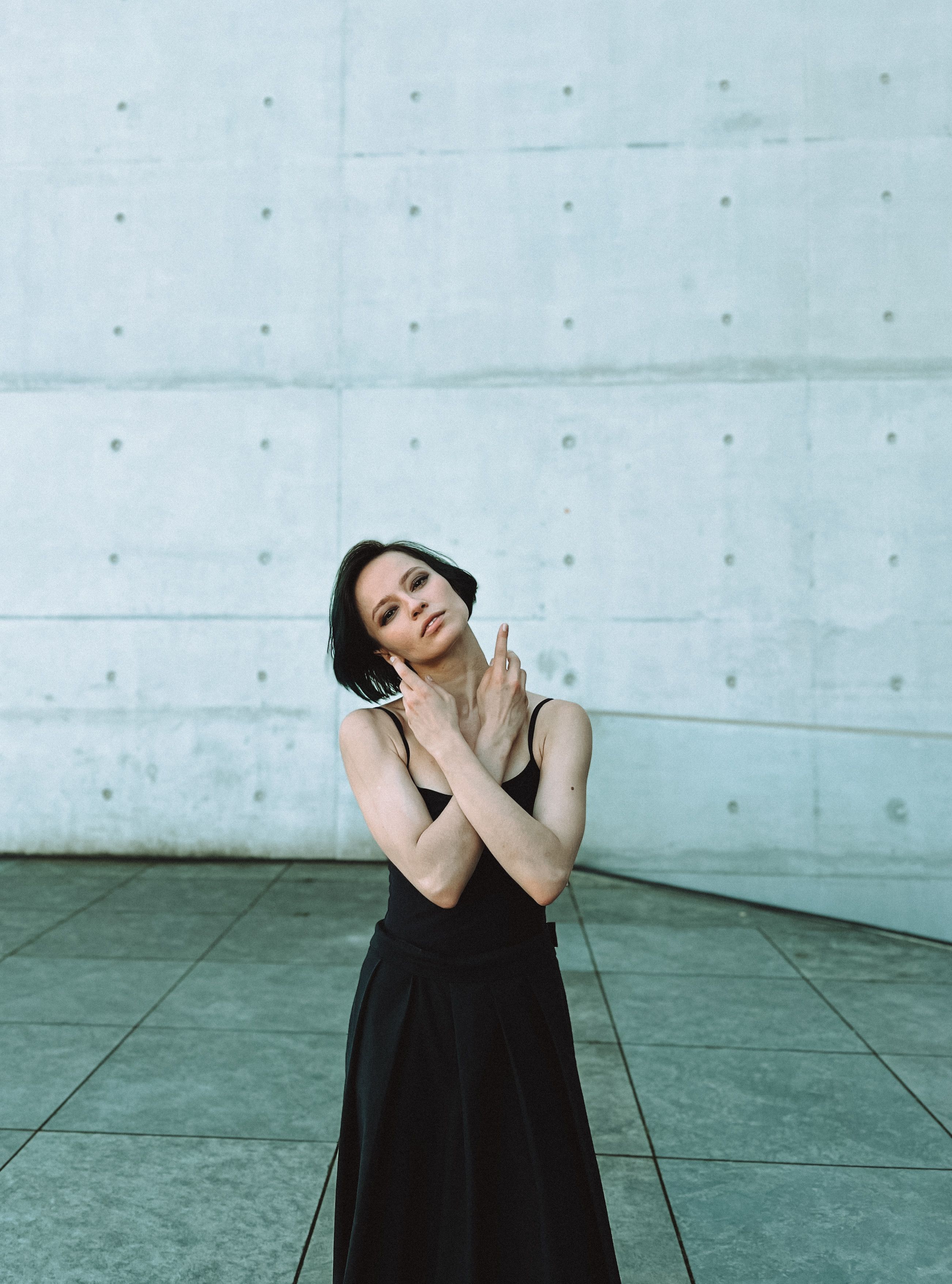 Stylish woman in black dress posing against concrete urban backdrop.