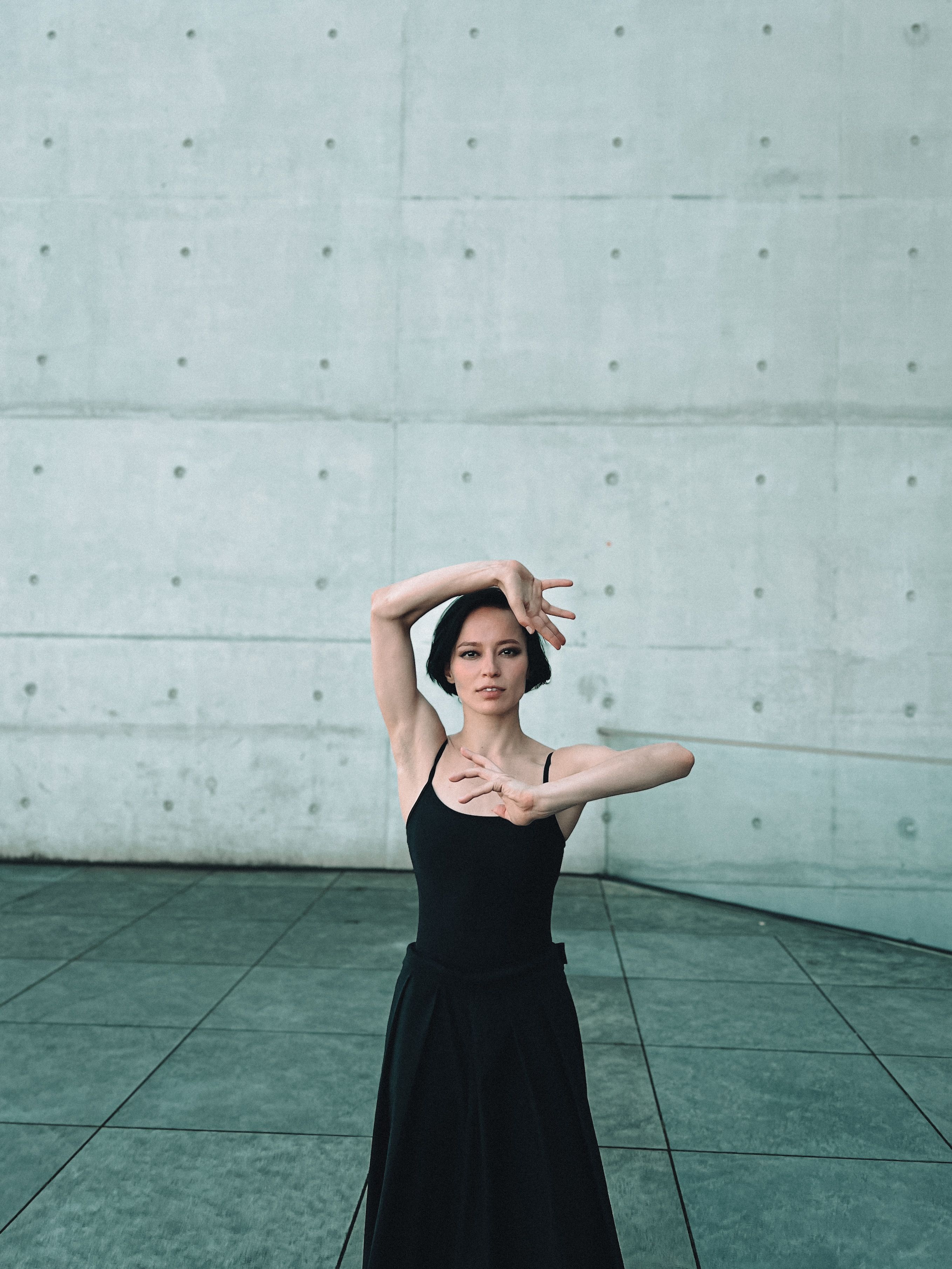 Woman in black dress striking a pose against an urban backdrop. Modern fashion photography.