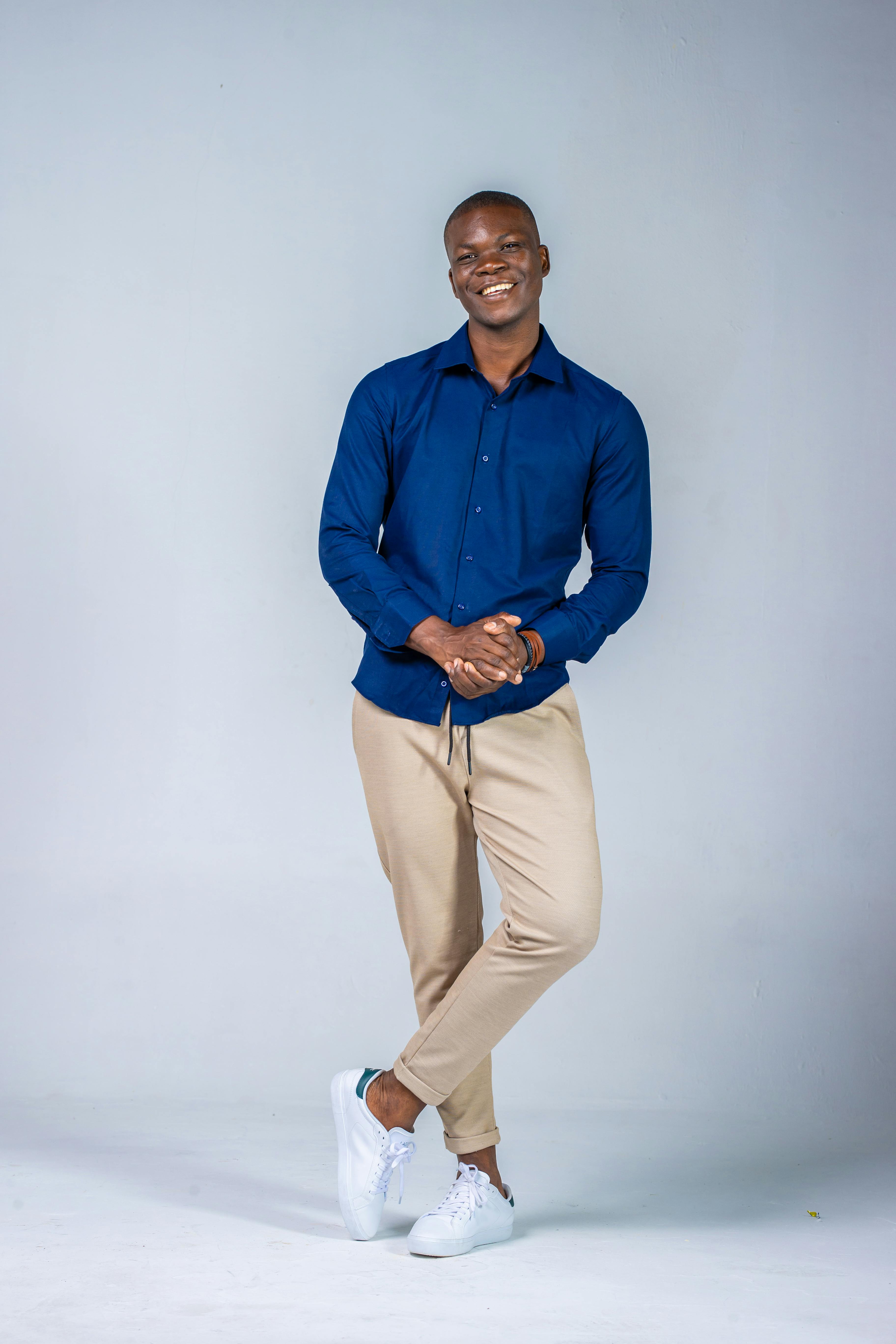 Portrait of a stylish male model in a blue shirt and beige pants, captured in a studio with a white background.