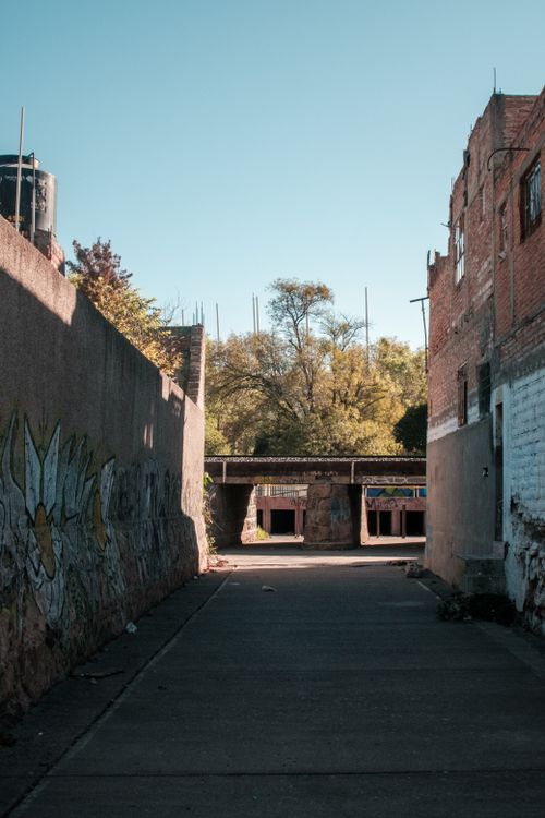 Free A city alley showcasing urban graffiti art leading to a bridge under a clear sky. Stock Photo