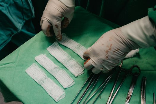 Surgeon's hands in gloves preparing bandages on a sterile field during surgery.