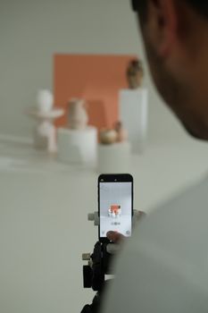 Photographer capturing minimalist still life with smartphone in studio setting.