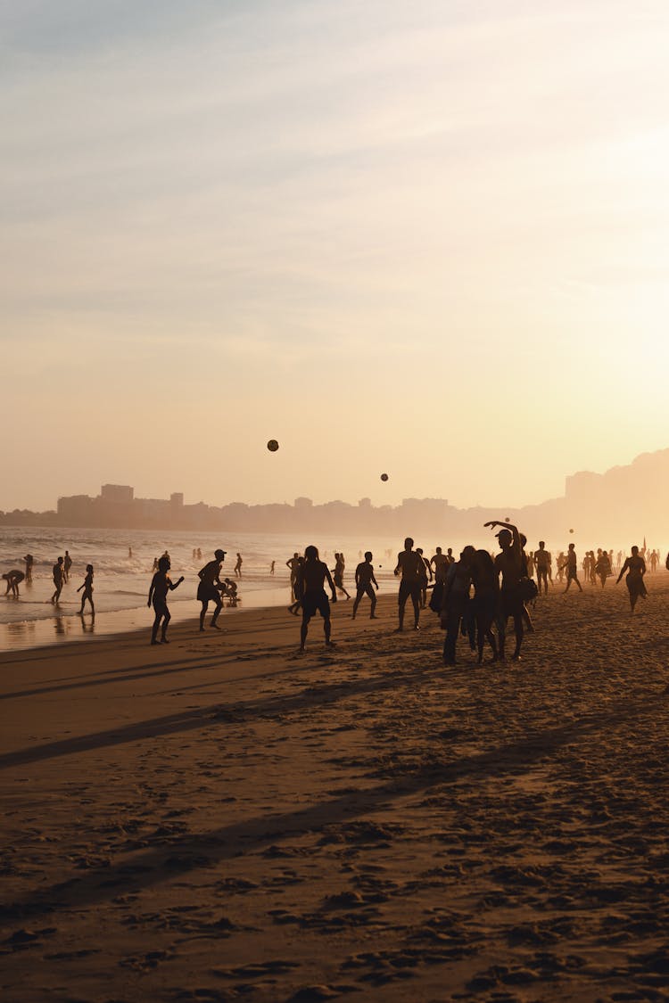 Silhouettes Of People Playing On The Beach At Sunset