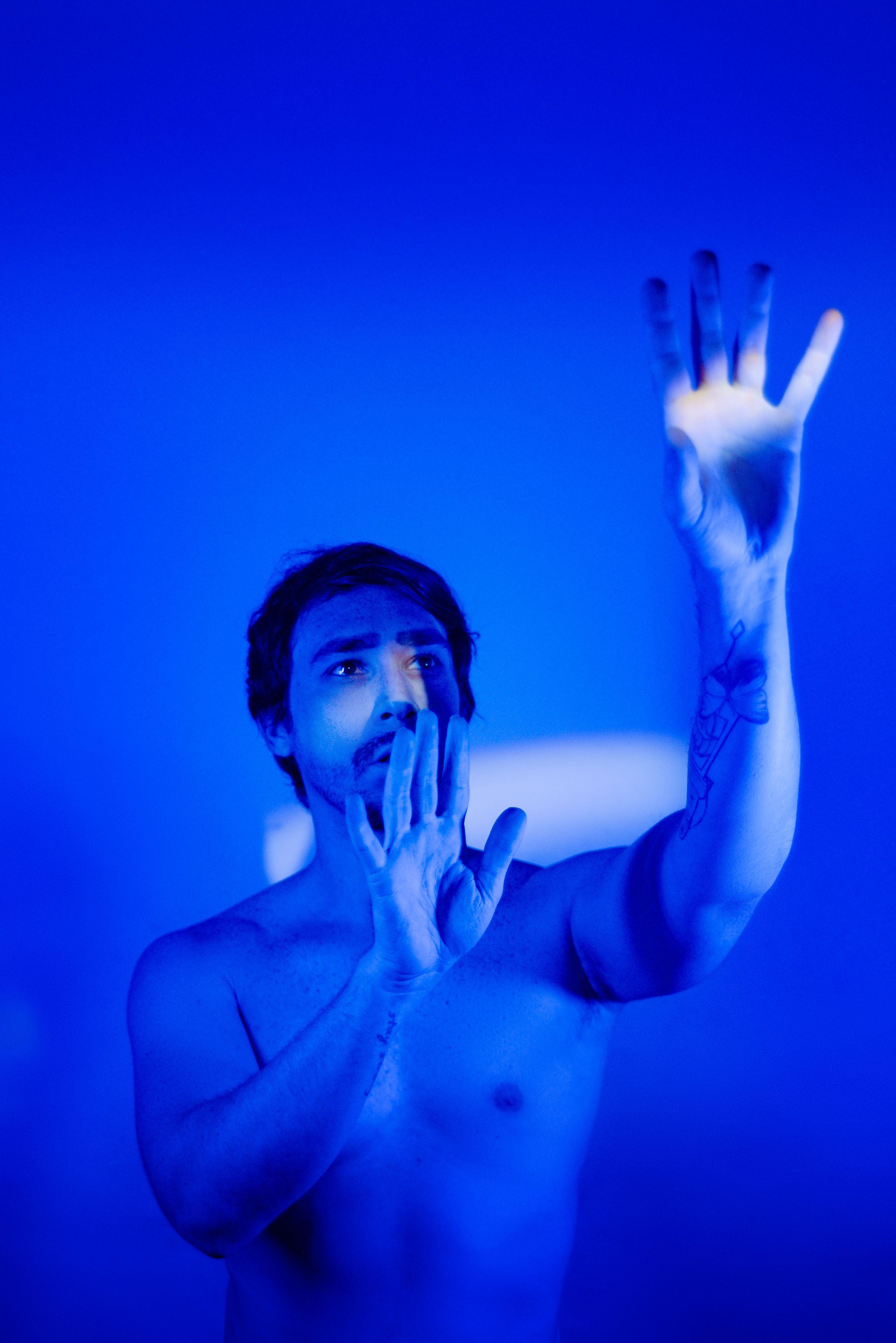 Dramatic studio portrait of a man with tattoos, featuring cool blue lighting and creative posing.