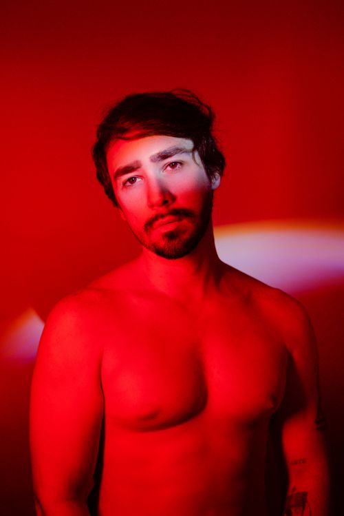 Free Striking studio portrait of a shirtless man with a beard under red lighting, showcasing intense expressions. Stock Photo