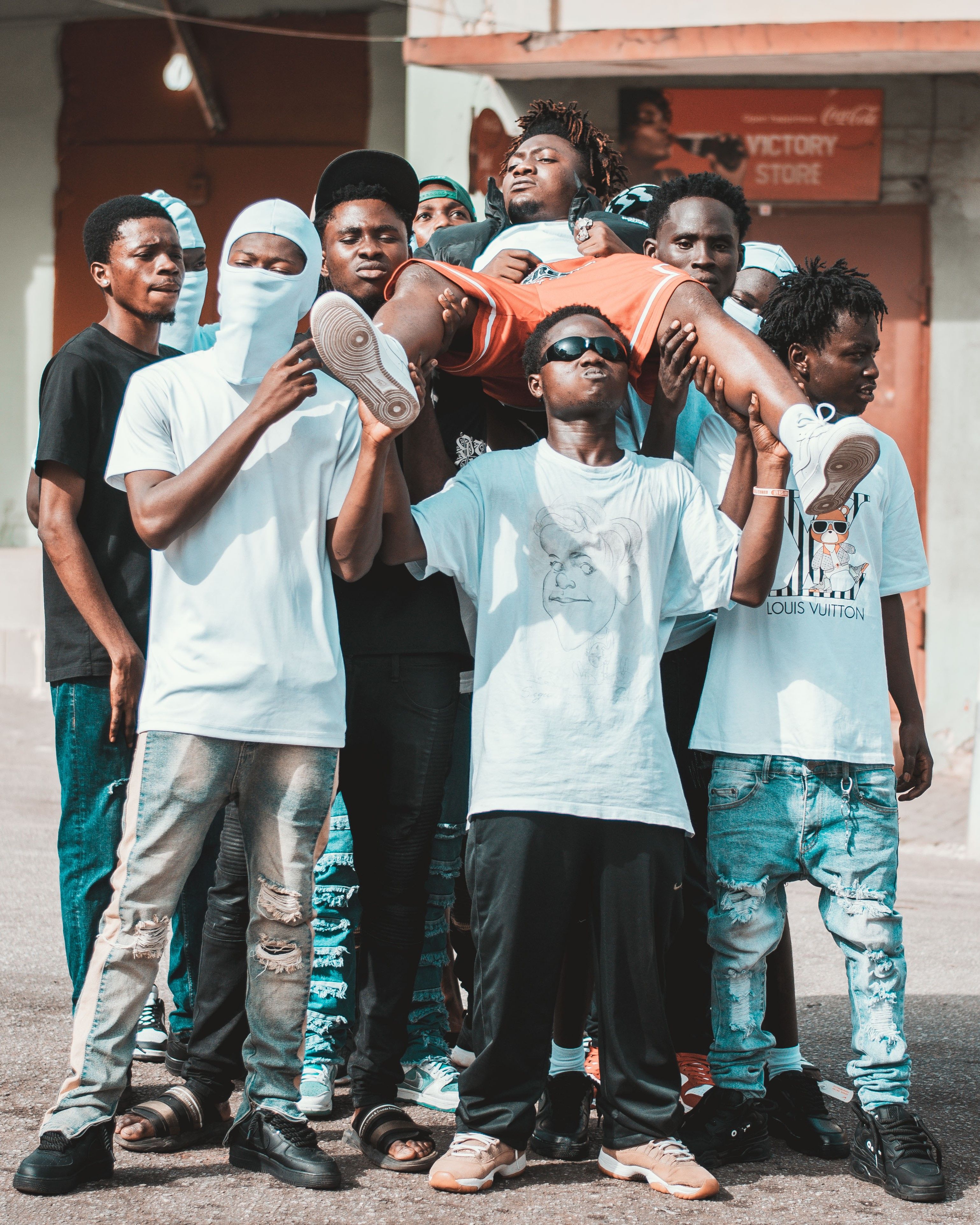 A group of stylish young men in streetwear gather in a sunny urban street in Kumasi.