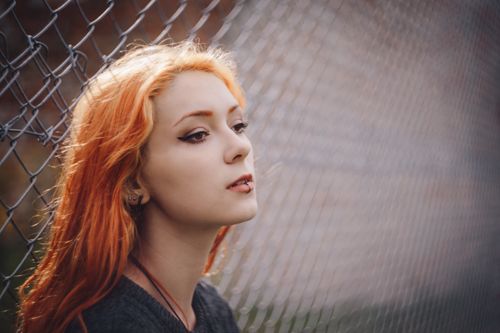 Free Captivating portrait of a woman with red hair and piercings near a wire fence. Stock Photo