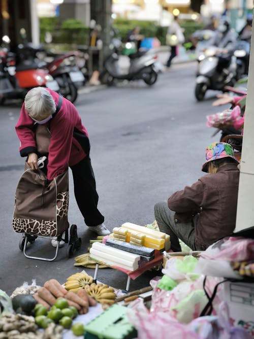 Free An elderly woman shops at an outdoor market, showcasing vibrant street commerce. Stock Photo