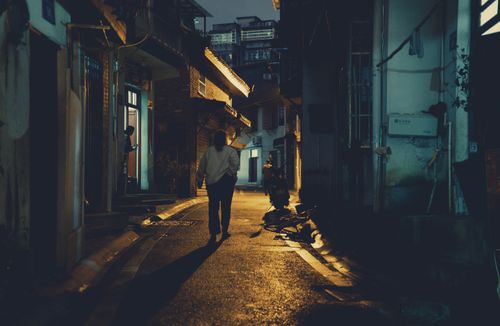 Free Mysterious figure walks through a dimly lit urban alley at night, creating a dramatic shadow. Stock Photo