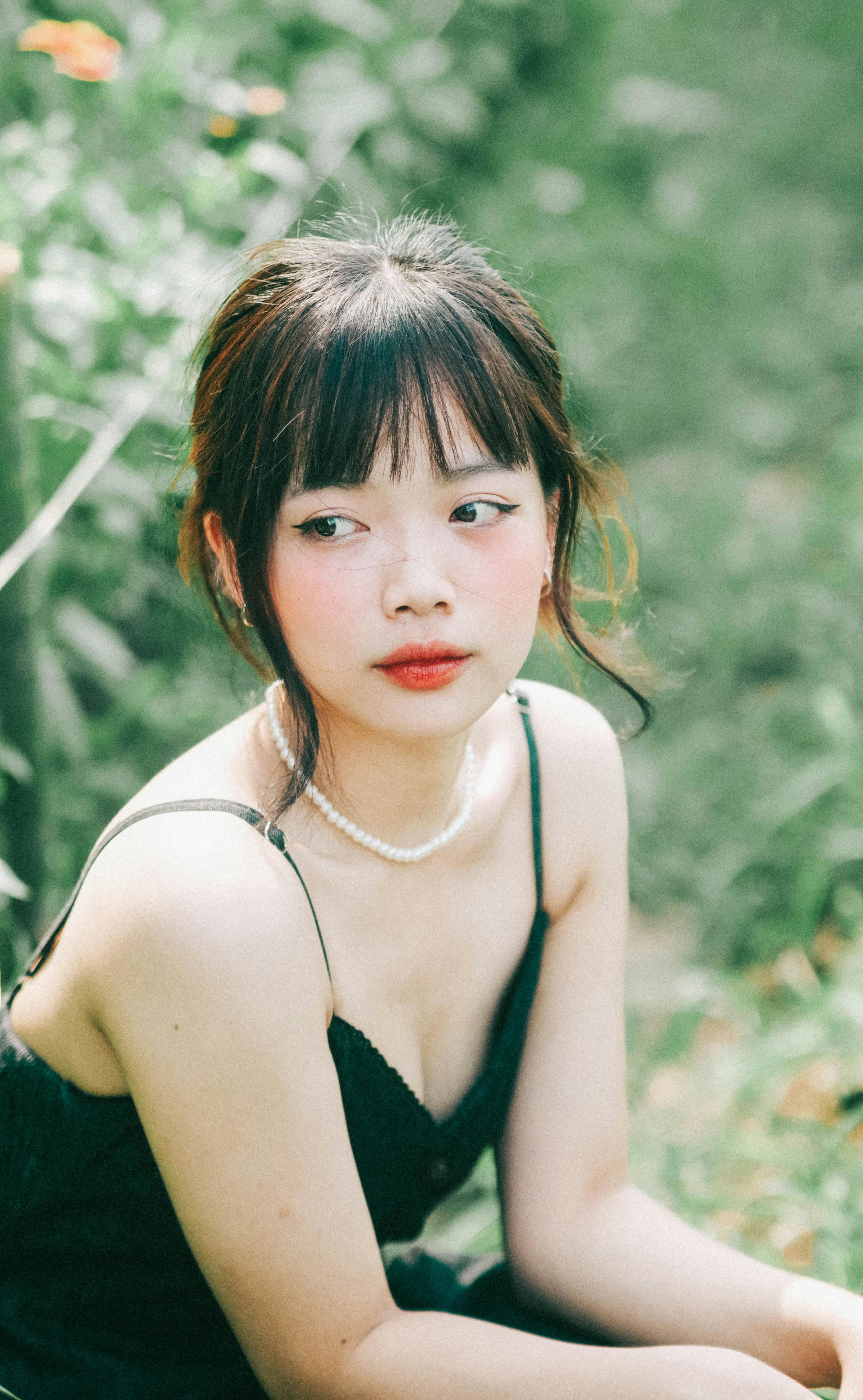 A serene portrait of a young woman with a pearl necklace, surrounded by greenery.