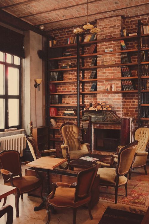 Free A vintage-style library room featuring armchairs, bookshelves, and a brick fireplace. Stock Photo