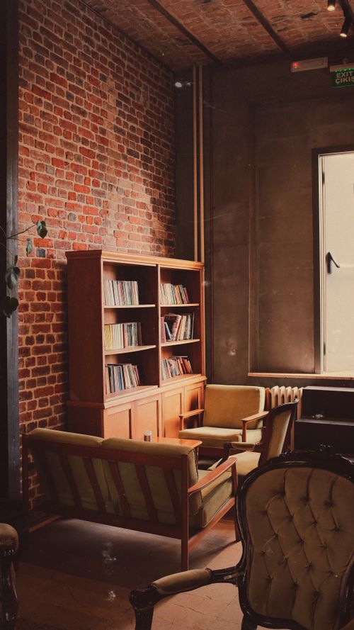 Free A cozy reading nook featuring armchairs, a bookshelf, and a rustic brick wall in a warmly lit interior. Stock Photo