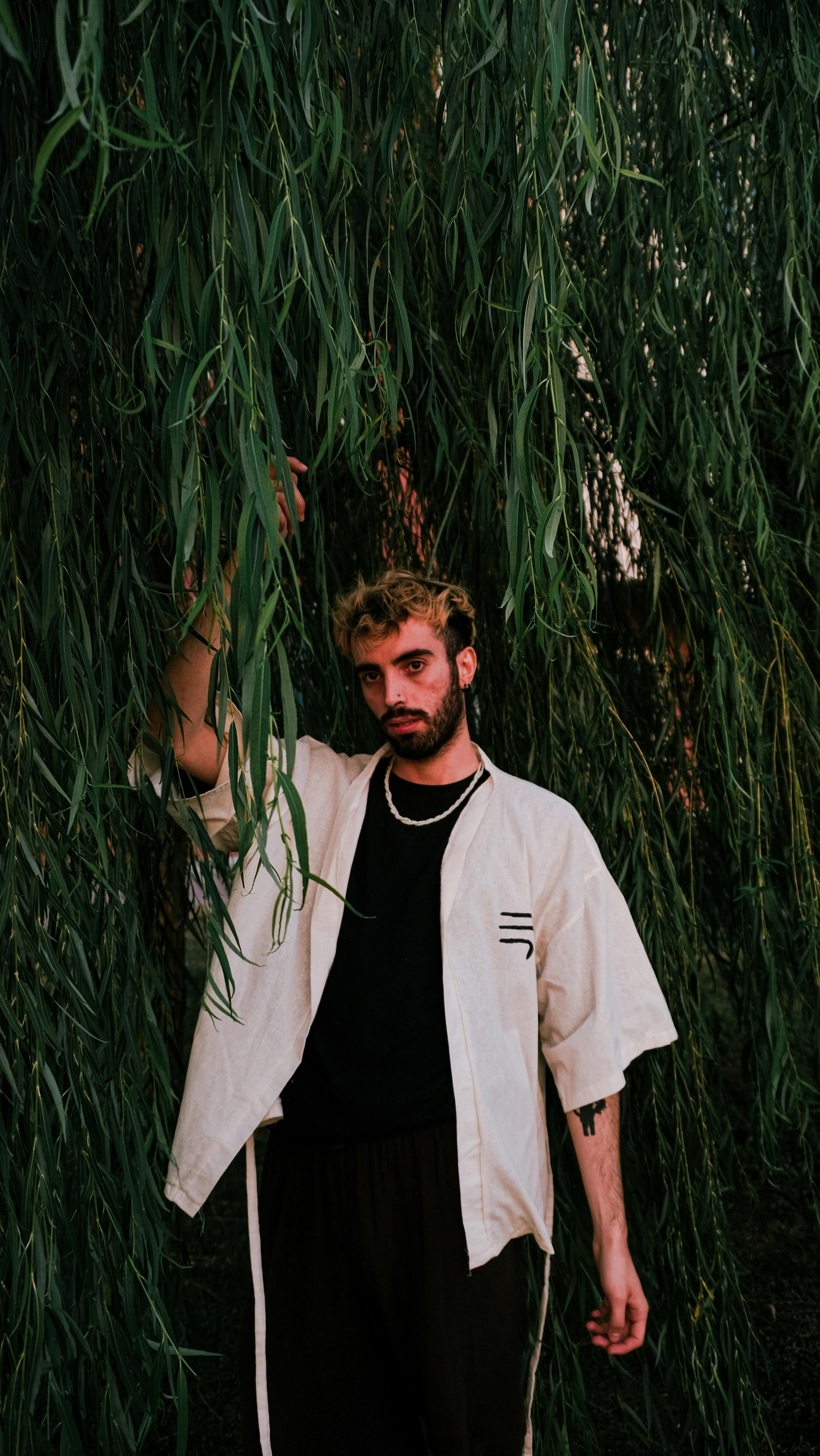 A stylish portrait of a man posing in a natural setting wearing a white kimono.