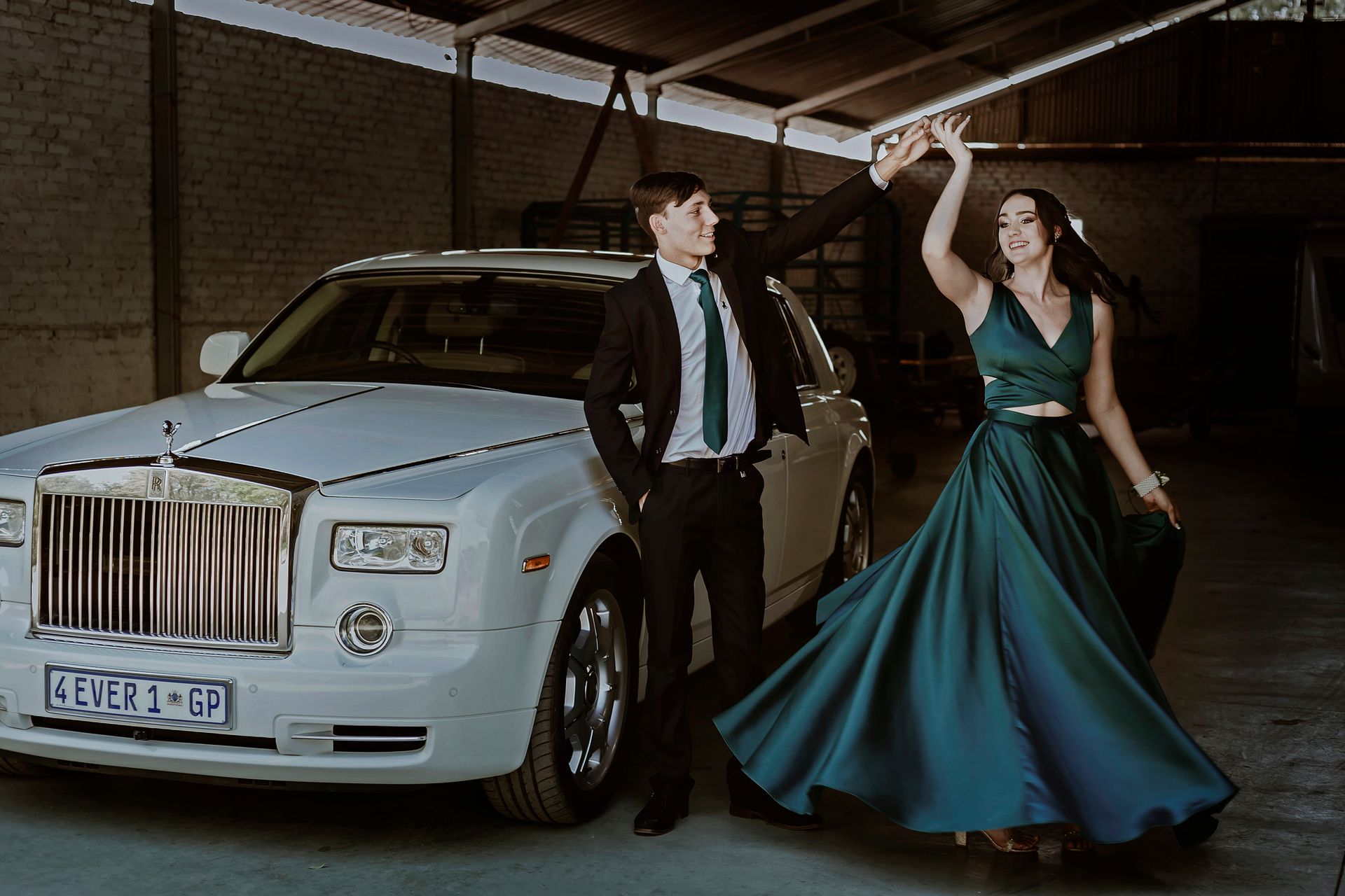 Stylish couple dancing beside a Rolls-Royce in a hangar setting, showcasing elegance and joy.
