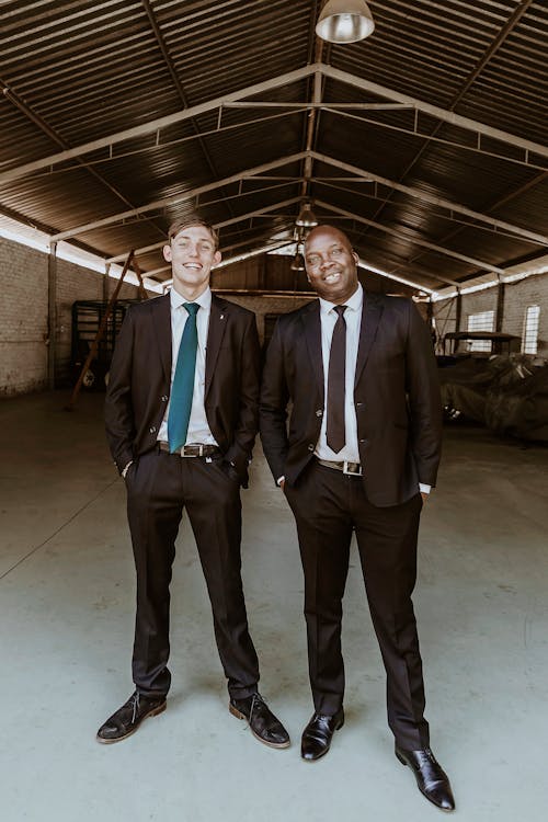 Two Men in Elegant Black Suits Standing in a Hangar