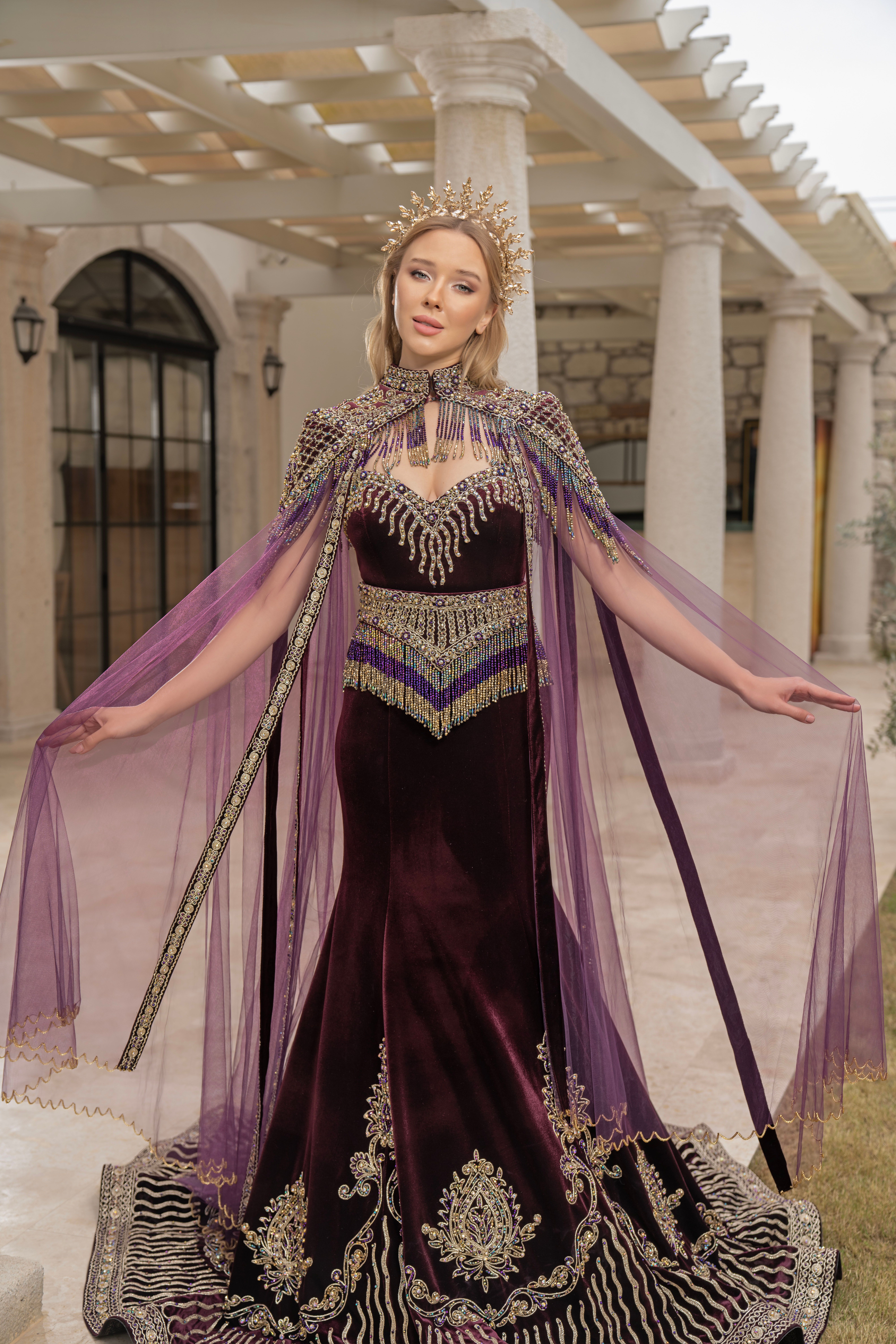 A woman in a stunning purple and silver gown stands gracefully in an elegant setting, exuding luxury and style.