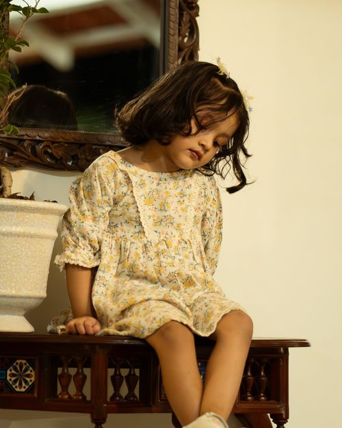 Free Charming young girl in floral dress sits by a decorative wooden cabinet indoors. Stock Photo
