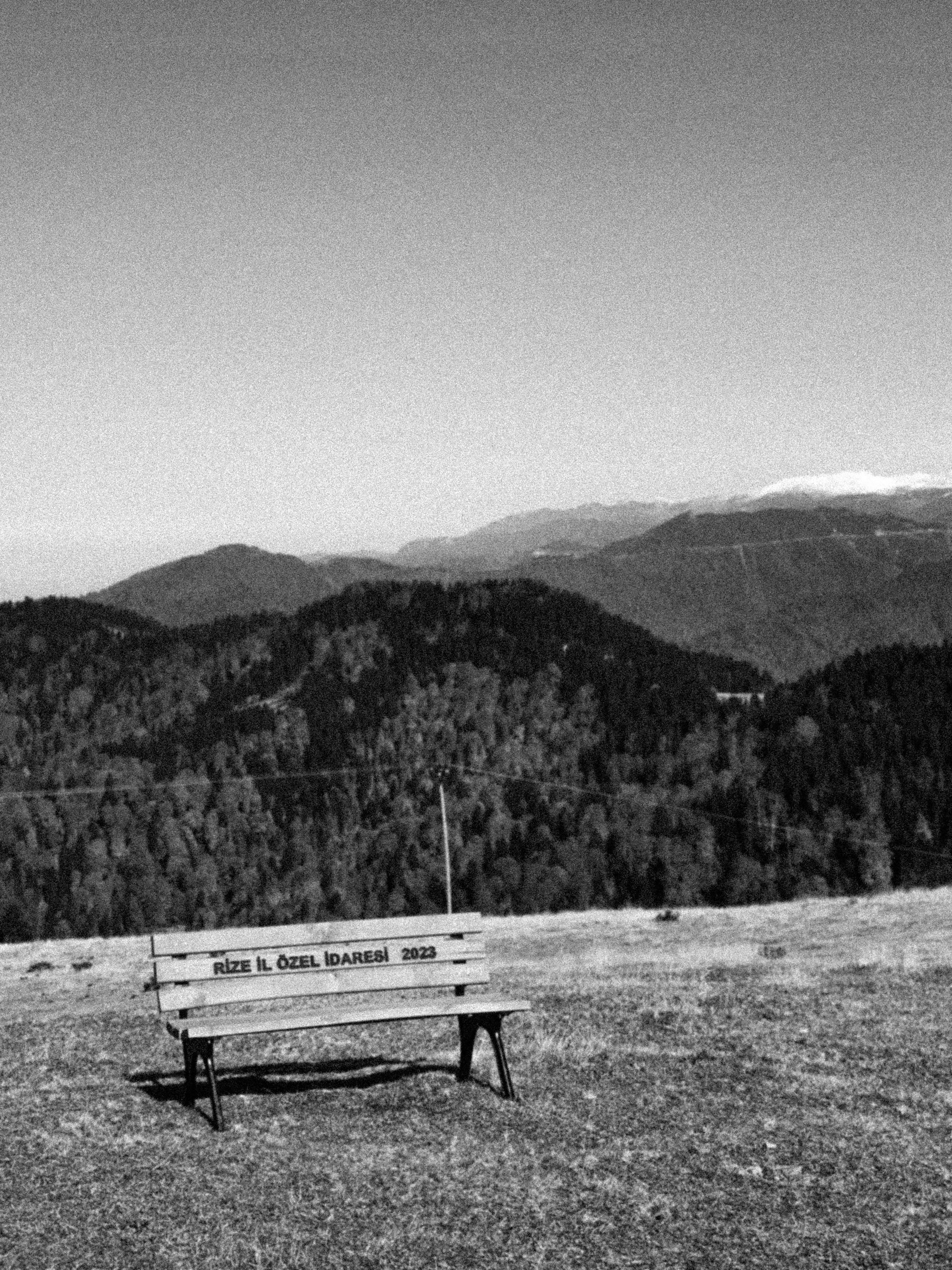 A black and white photo of a bench on a hillside in Rize, Türkiye, offering a panoramic mountain view.