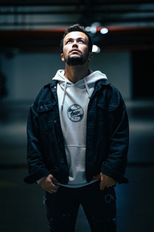 Free A man wearing a white hoodie and denim jacket looking up in a moody, dimly lit garage setting. Stock Photo