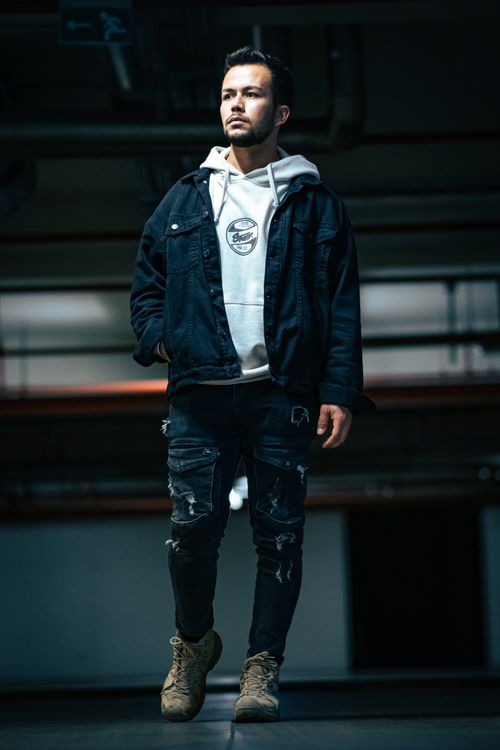 Free Stylish male model posing in an underground parking lot wearing a denim jacket and white hoodie. Stock Photo
