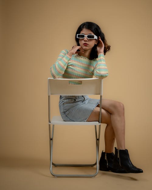 Young Model in a Striped Sweater and Denim Mini Skirt Sitting on a Chair