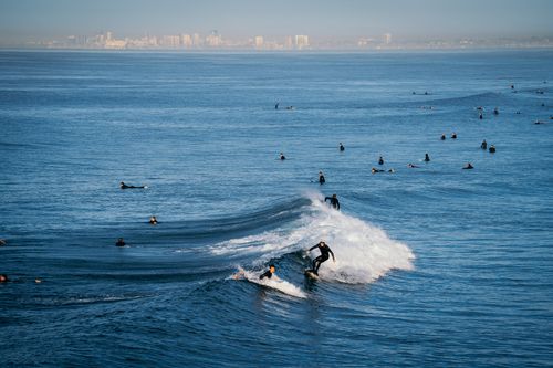 Free A group of surfers enjoying the waves with a city skyline in the background, perfect for travel and sports themes. Stock Photo