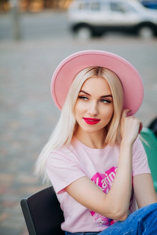 Young Woman in a Pink T-shirt and Hat Sitting Outside 