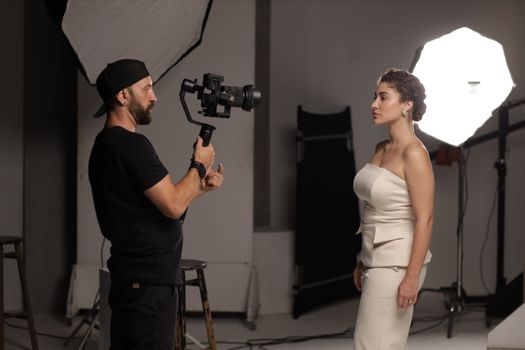 A studio portrait session featuring a model in elegant attire and a photographer with a camcorder.