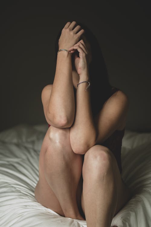Woman Covering Face Through Hands Sitting on Bed