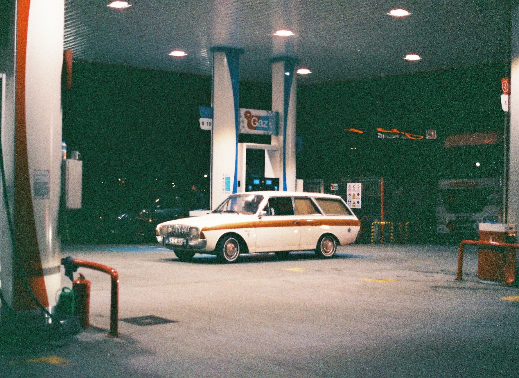 A classic vintage car parked at an illuminated gas station in Istanbul, Türkiye, at night.