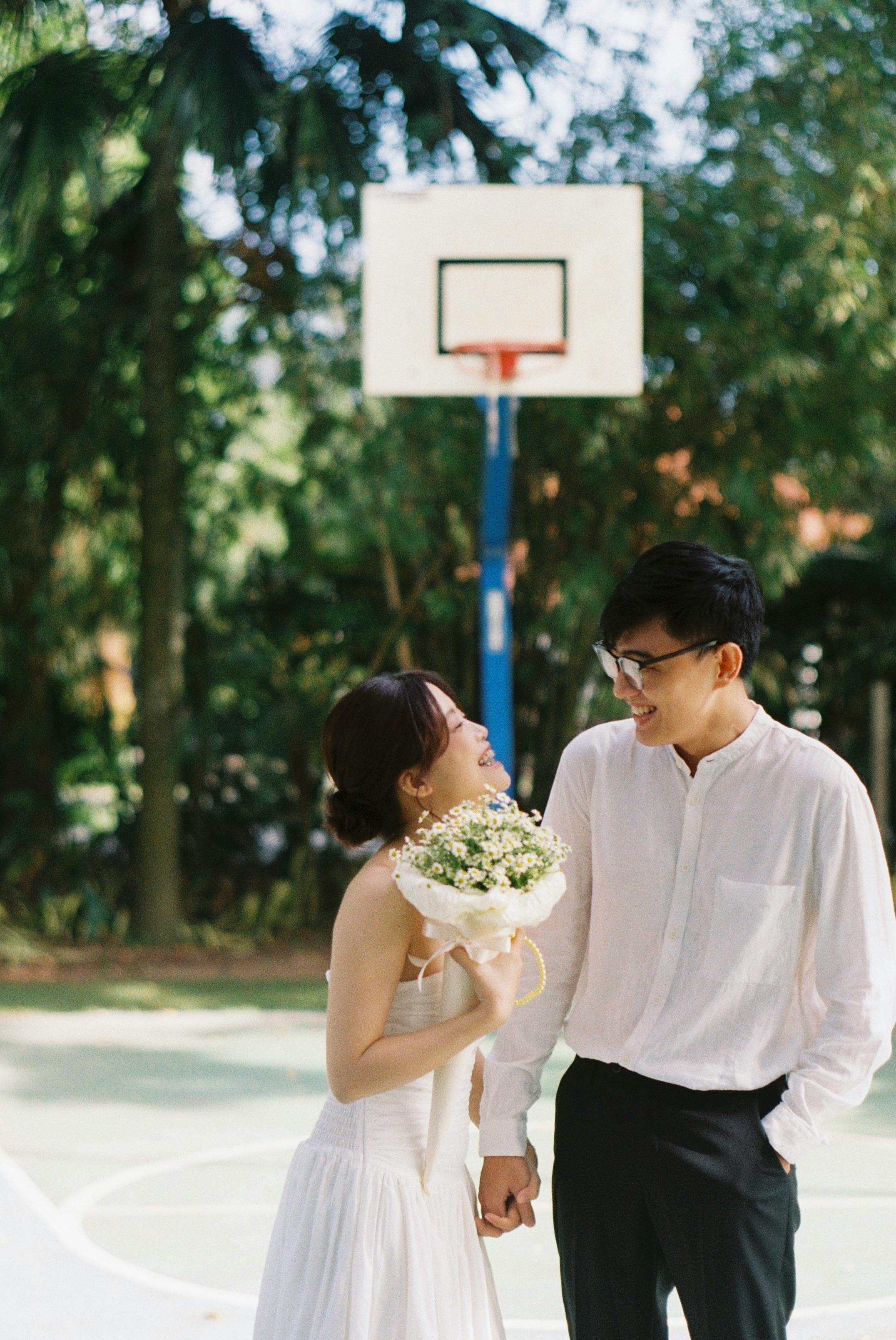 An Asian couple celebrating romance at an outdoor park basketball court.