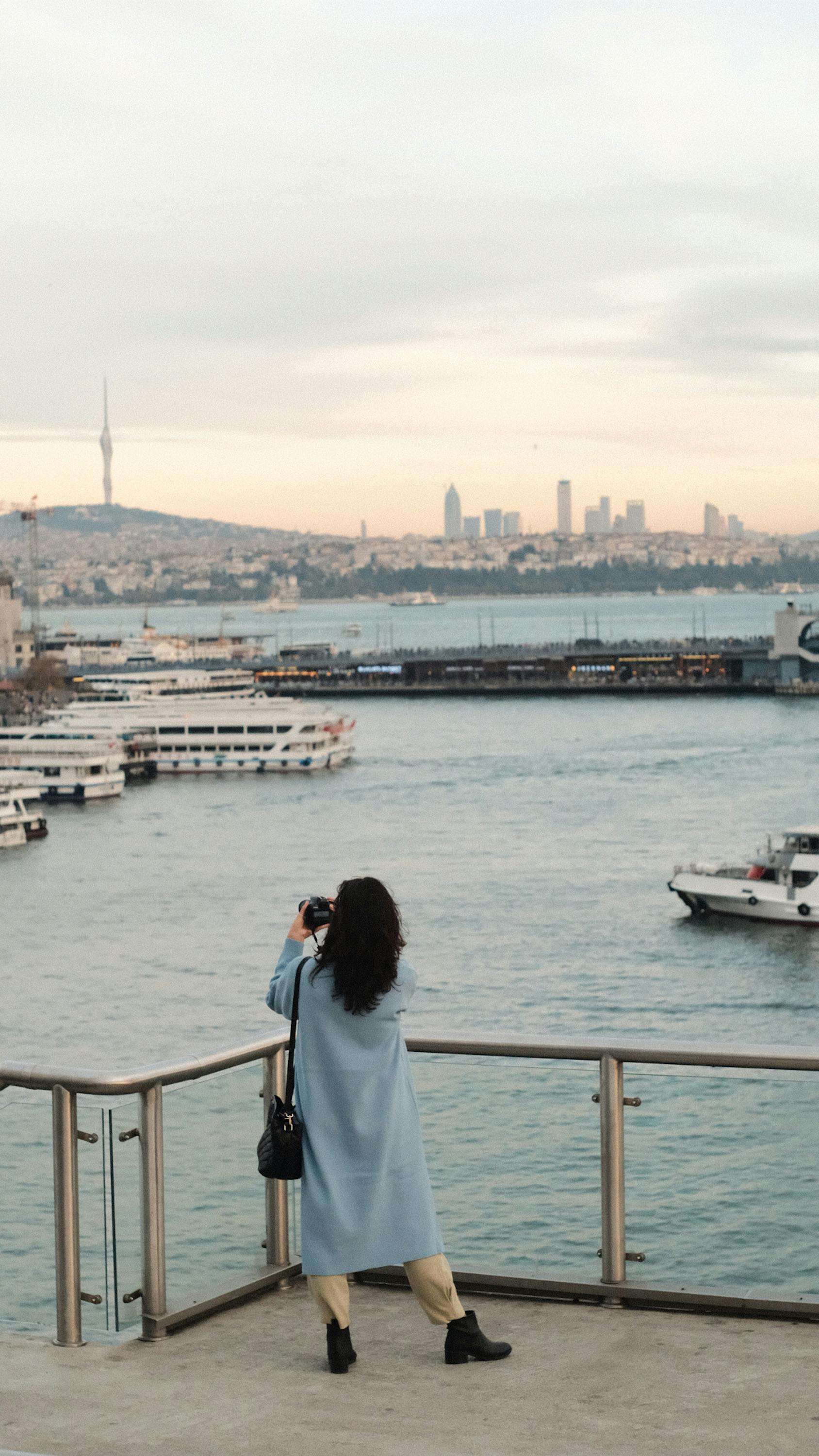 Woman enjoys the scenic view of a harbor at sunset, capturing the skyline with her camera.