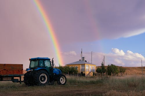 A Tractor on a Field under a Sky with a Rainbow 