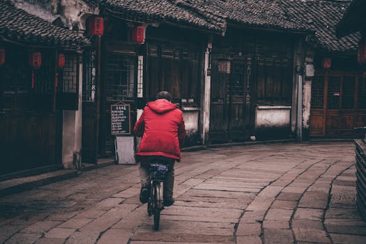 一个穿着红色外套的男人骑着自行车穿过一条有着经典建筑的老式街道