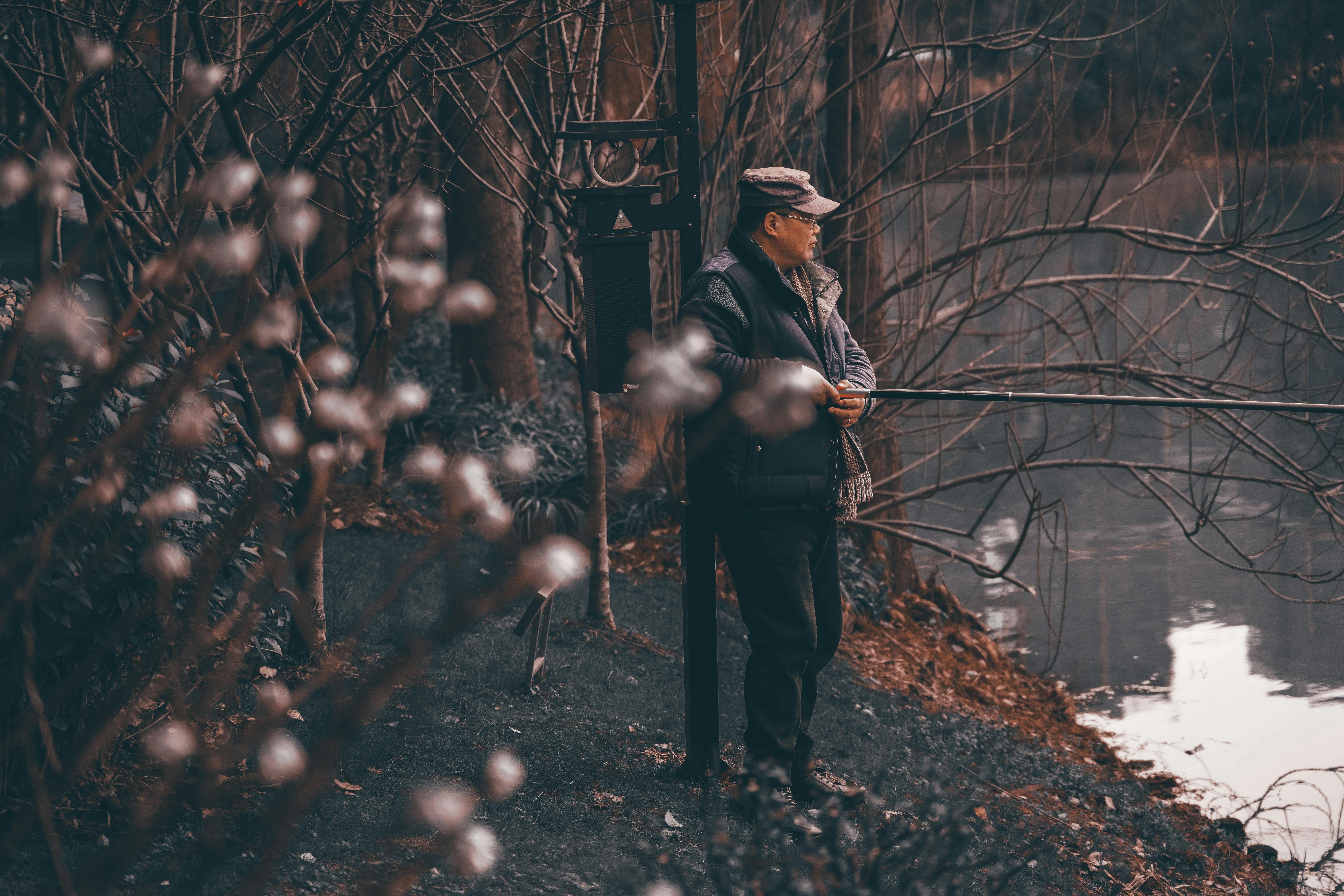 一个穿着冬装的男人在光秃秃的树木间，静静欣赏着湖畔景色