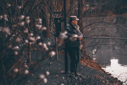 一个穿着冬装的男人在光秃秃的树木间，静静欣赏着湖畔景色