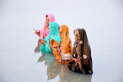Indian women participate in a traditional water ceremony wearing colorful saris, reflecting cultural reverence.