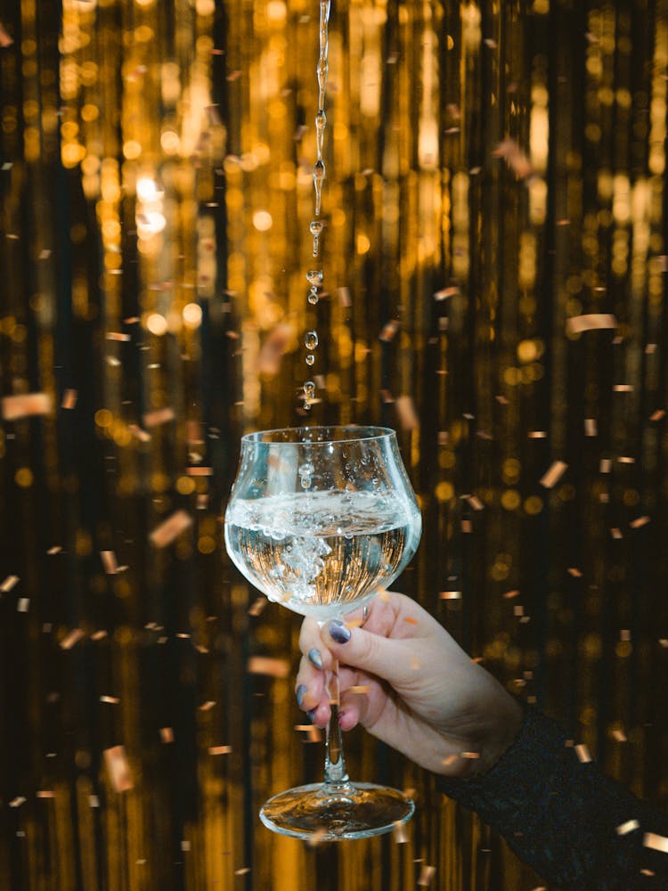 Pouring Water Into A Wineglass On The Background Of A Golden Curtain