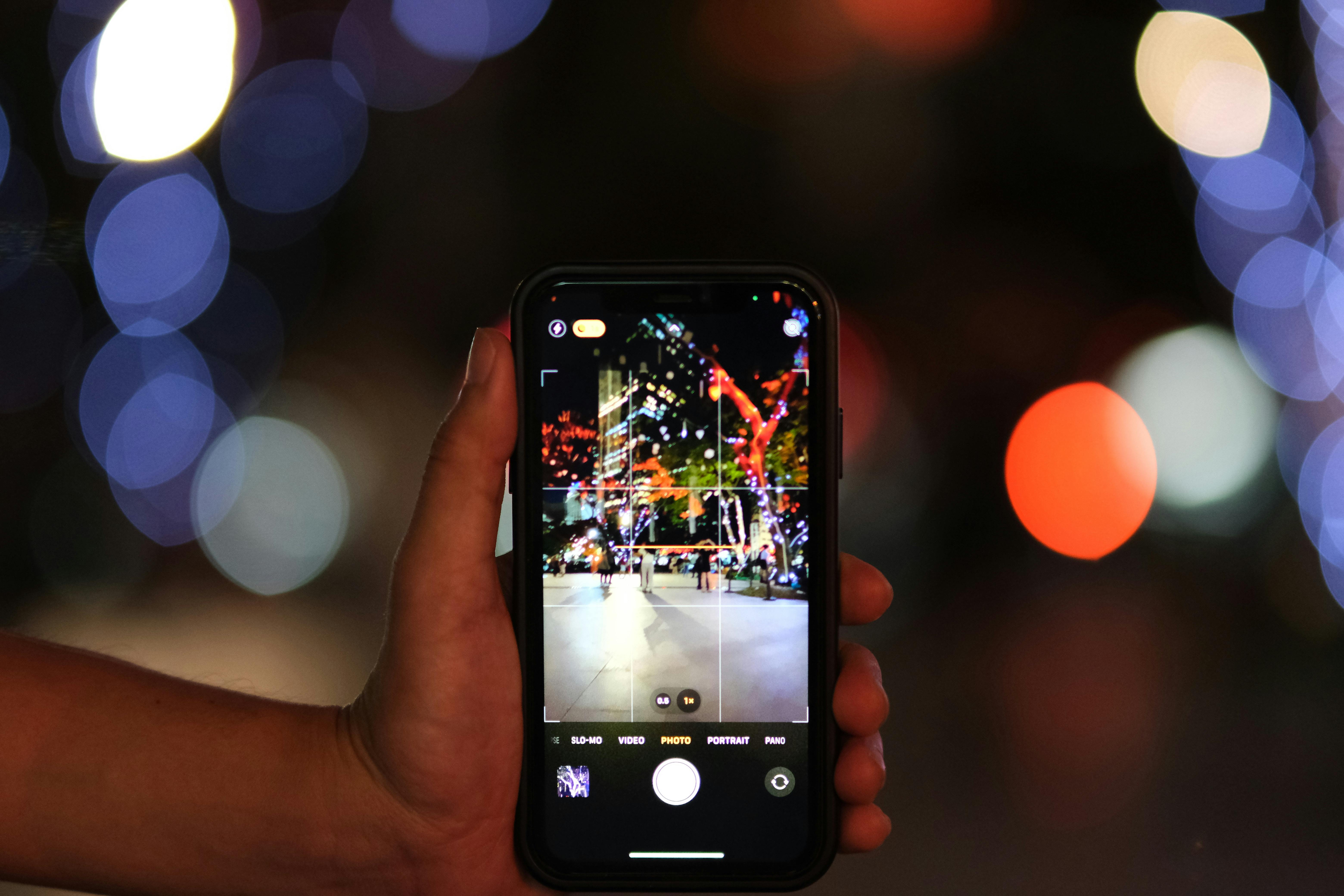 Free Close-up of a smartphone capturing a vibrant city scene with colorful bokeh lights at night. Stock Photo