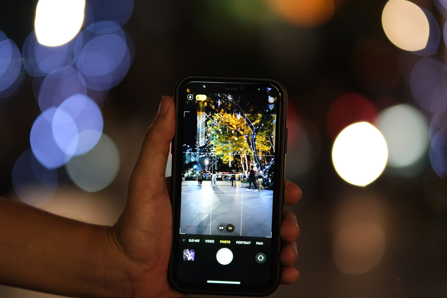 Vibrant image of a smartphone photographing a bustling night scene with bokeh effect.