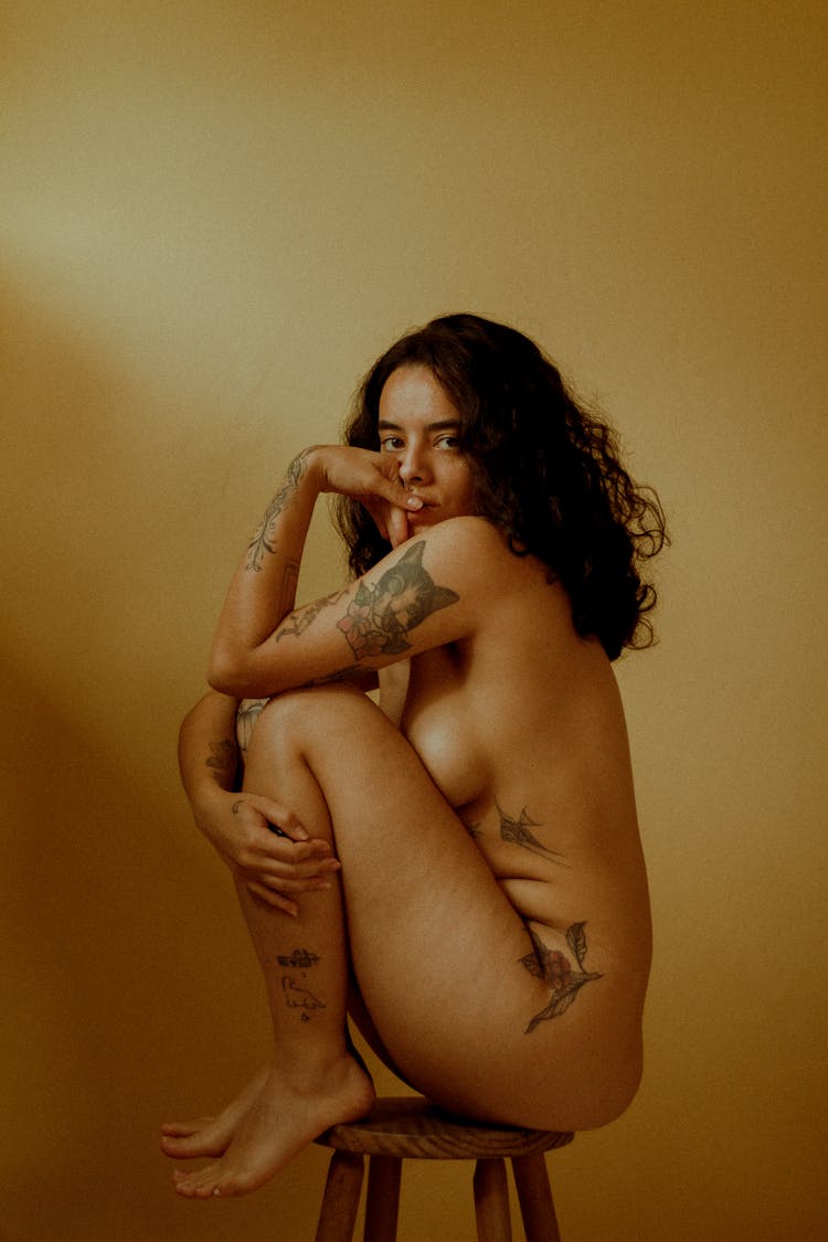 Young Naked Woman With Tattoo On Her Body Sitting On A Stool 