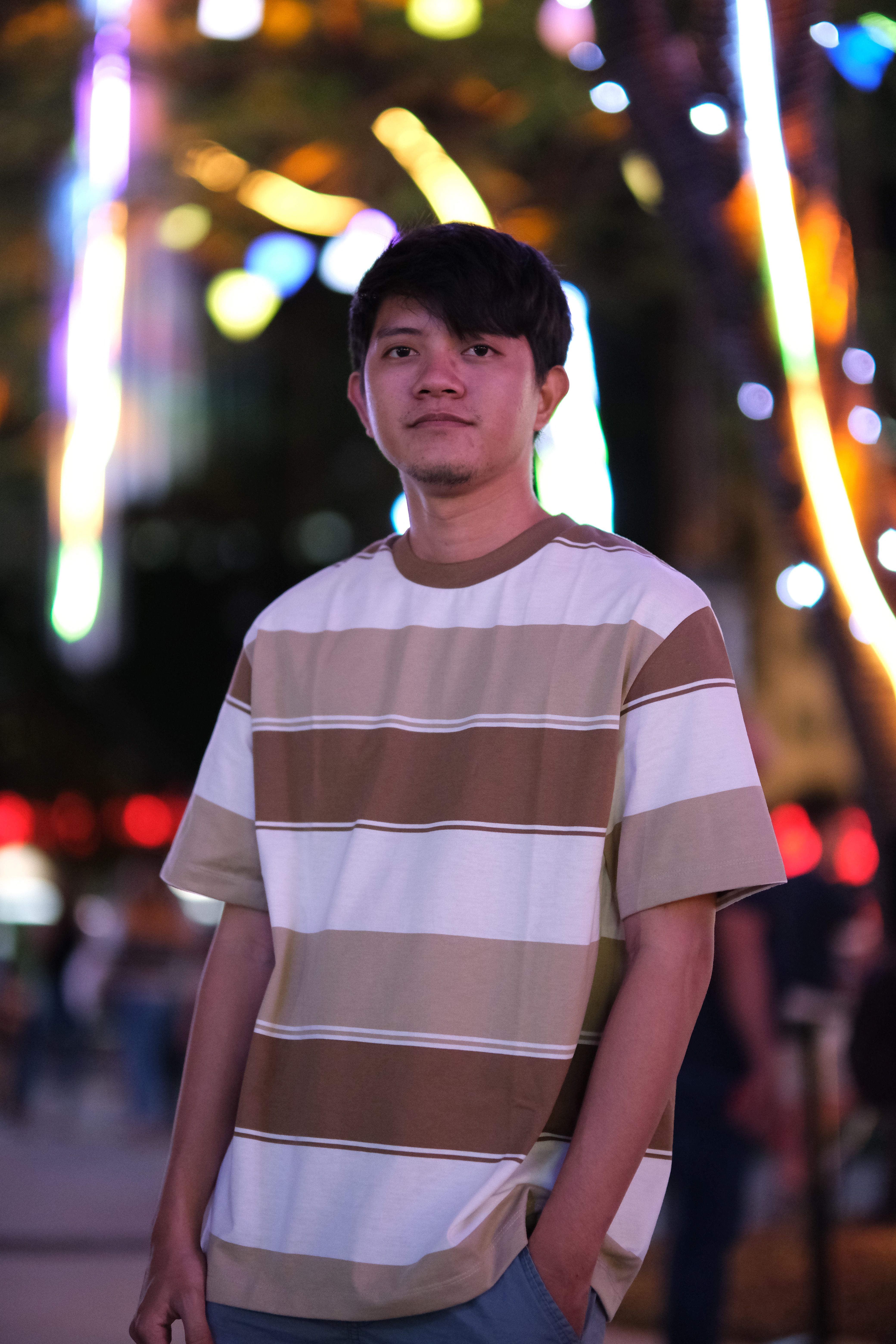 Young man in casual attire at night with bokeh city lights.
