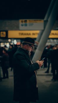 Man in dark coat and hat using phone at a bustling train station, capturing the essence of urban life.