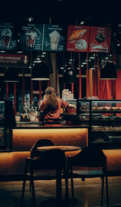 Free Warmly lit café with a barista working behind the counter, creating an inviting atmosphere. Stock Photo