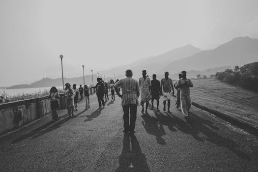 A group of people walk on a pathway in silhouette against majestic mountain backdrop in Wayanad.