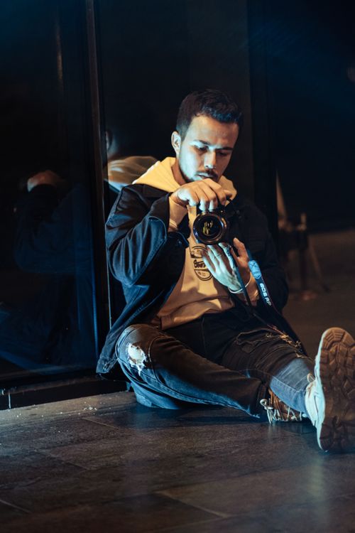 Free A young man sitting on the floor indoors, holding and examining a camera. Stock Photo