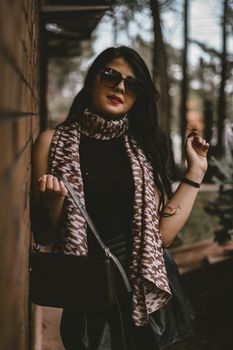 Chic woman with black hair and sunglasses posing outdoors, exuding modern fashion sense.